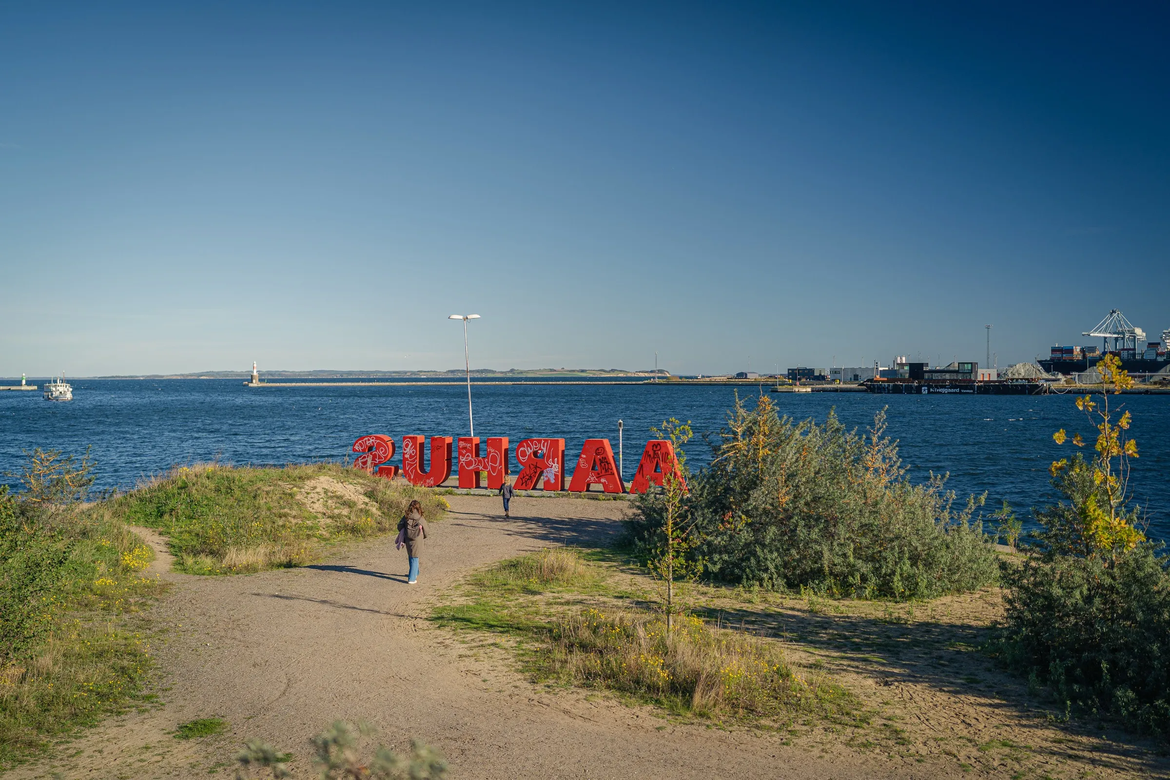 A path across a meadow to large red letters at the tip of the pier, the sea behind