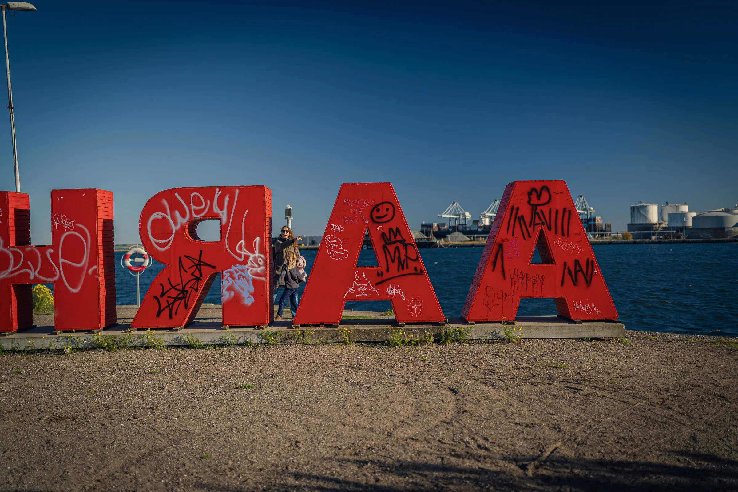 Red wooden letters with graffiti by the water, seen from behind