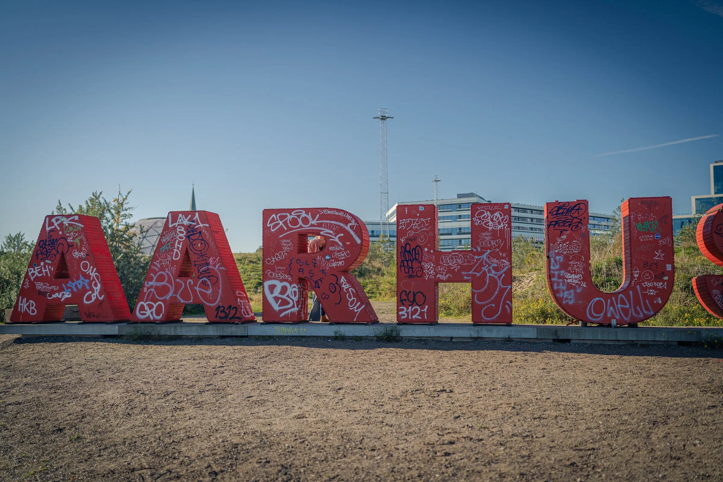 The red letters AARHUS with graffiti on a gravel area
