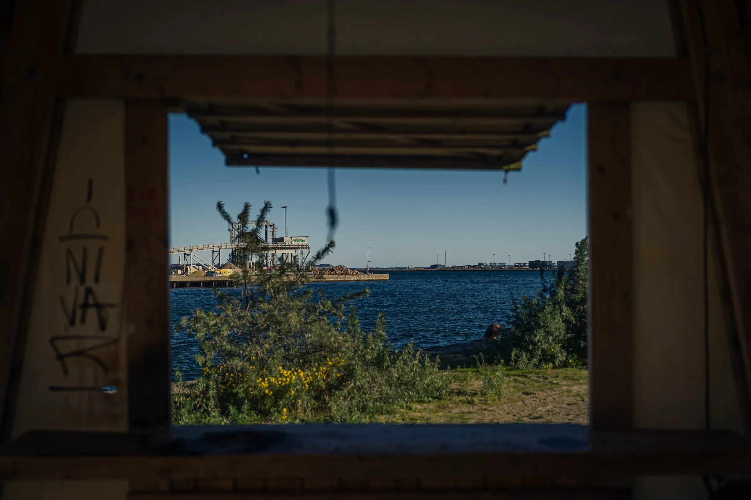 A dark wooden frame through which you look at water and a crane