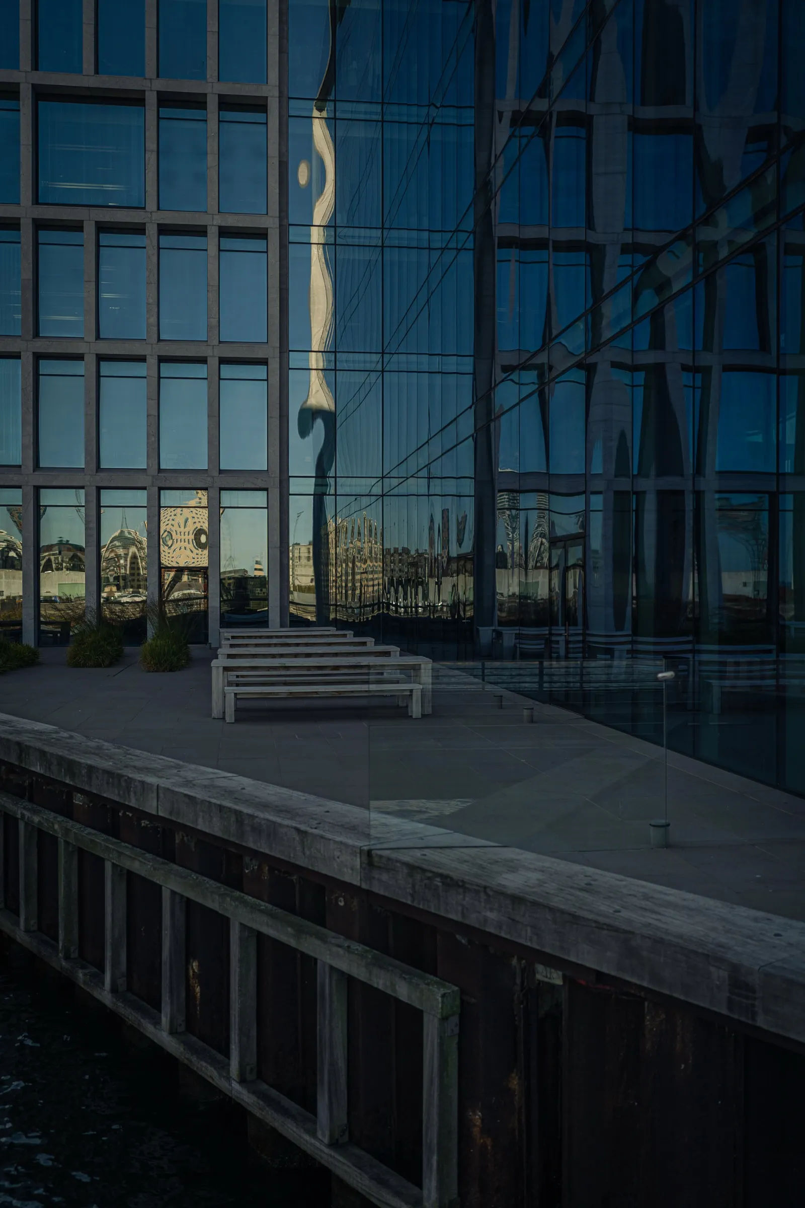 Portrait: a dark glass facade above a quay wall by the water