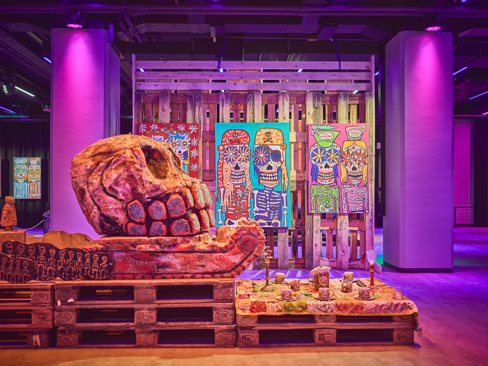 Two large skeleton figures made of painted wood, one on a motorcycle, in violet exhibition light