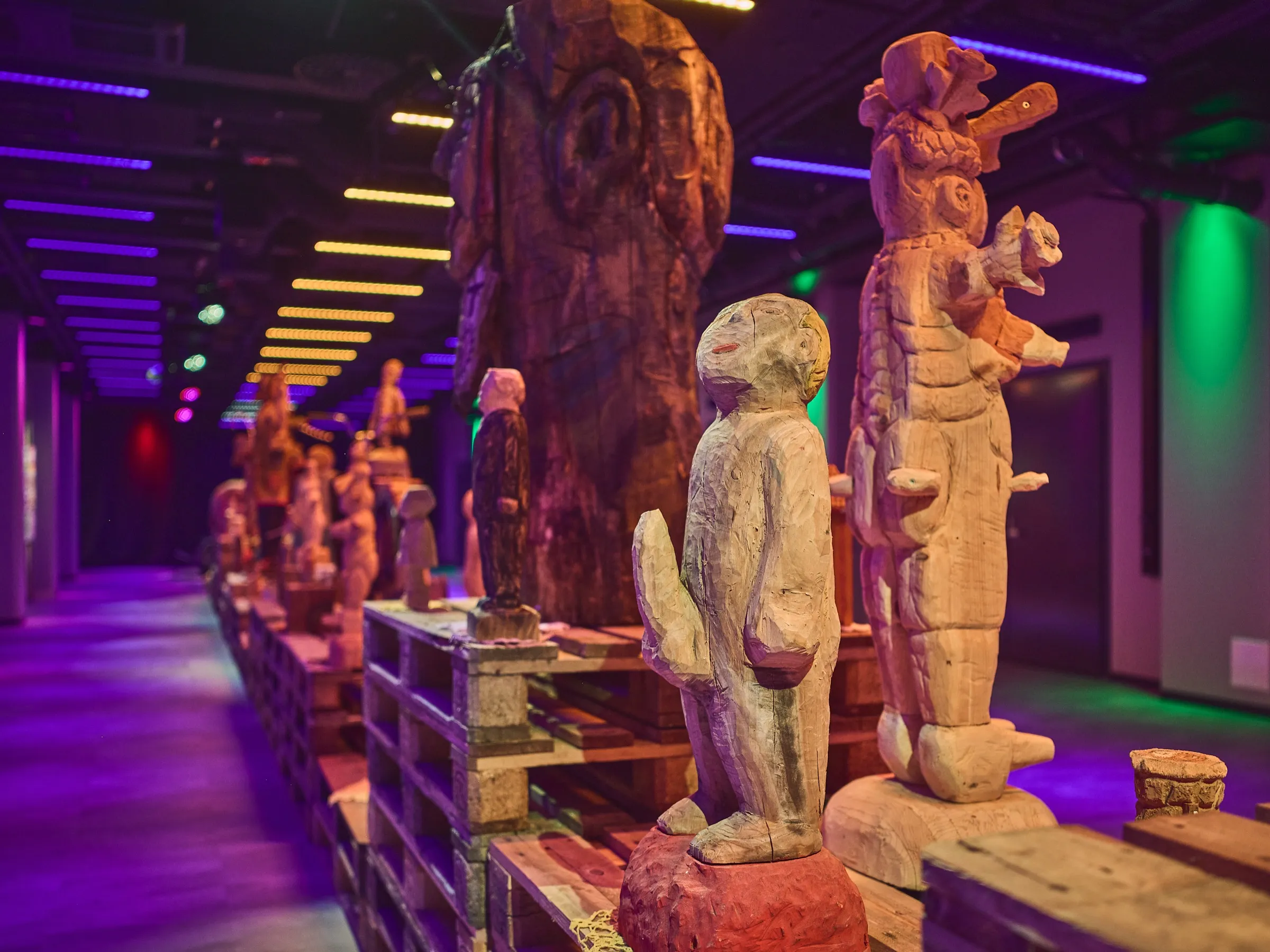 Row of raw, unpainted wooden figures along a dark aisle