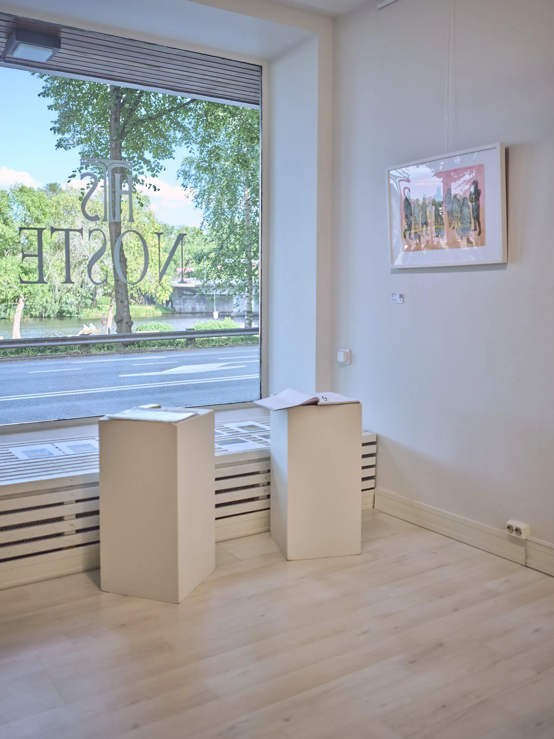 Two white plinths in front of the gallery's shop window, street and trees outside, portrait format