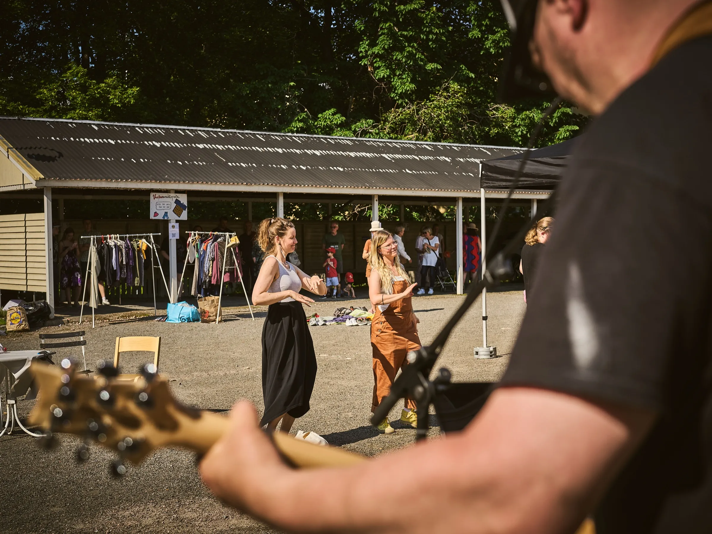Two women dancing in front of the racks of the clothing swap station, a bassist in the foreground