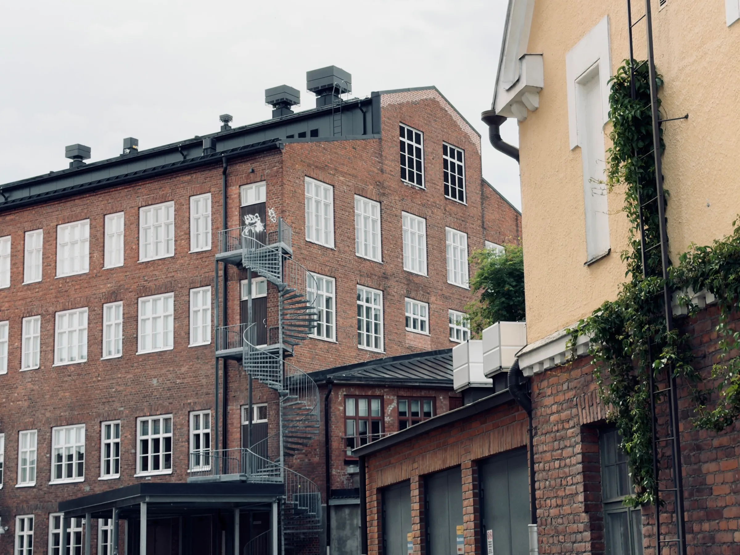 Long red brick facade of the former cloth mill with a spiral staircase, the yellow gable on the right