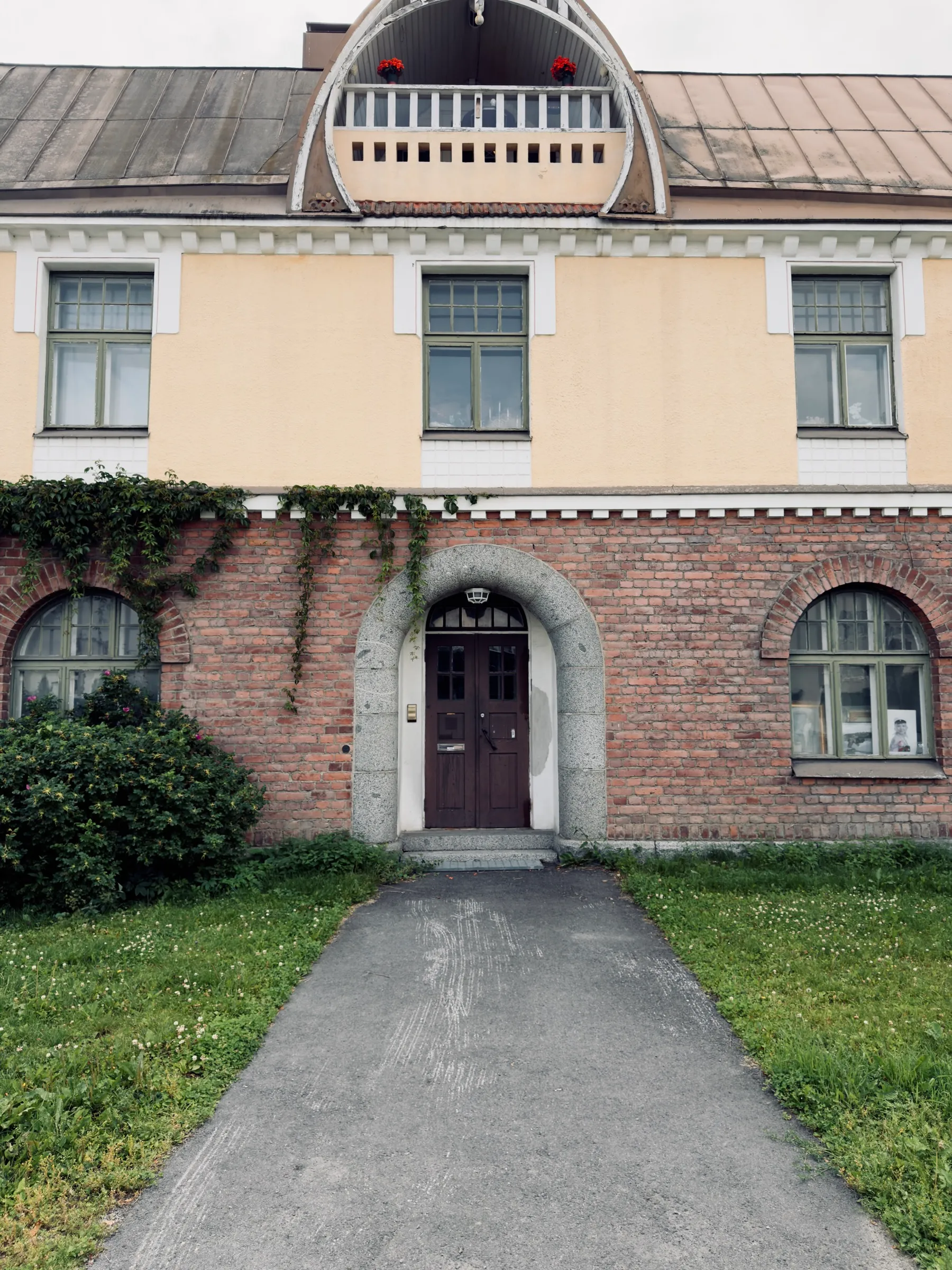 Front view of the Verkatehdas office gable: yellow plaster above red brick, curved Jugendstil gable with balcony