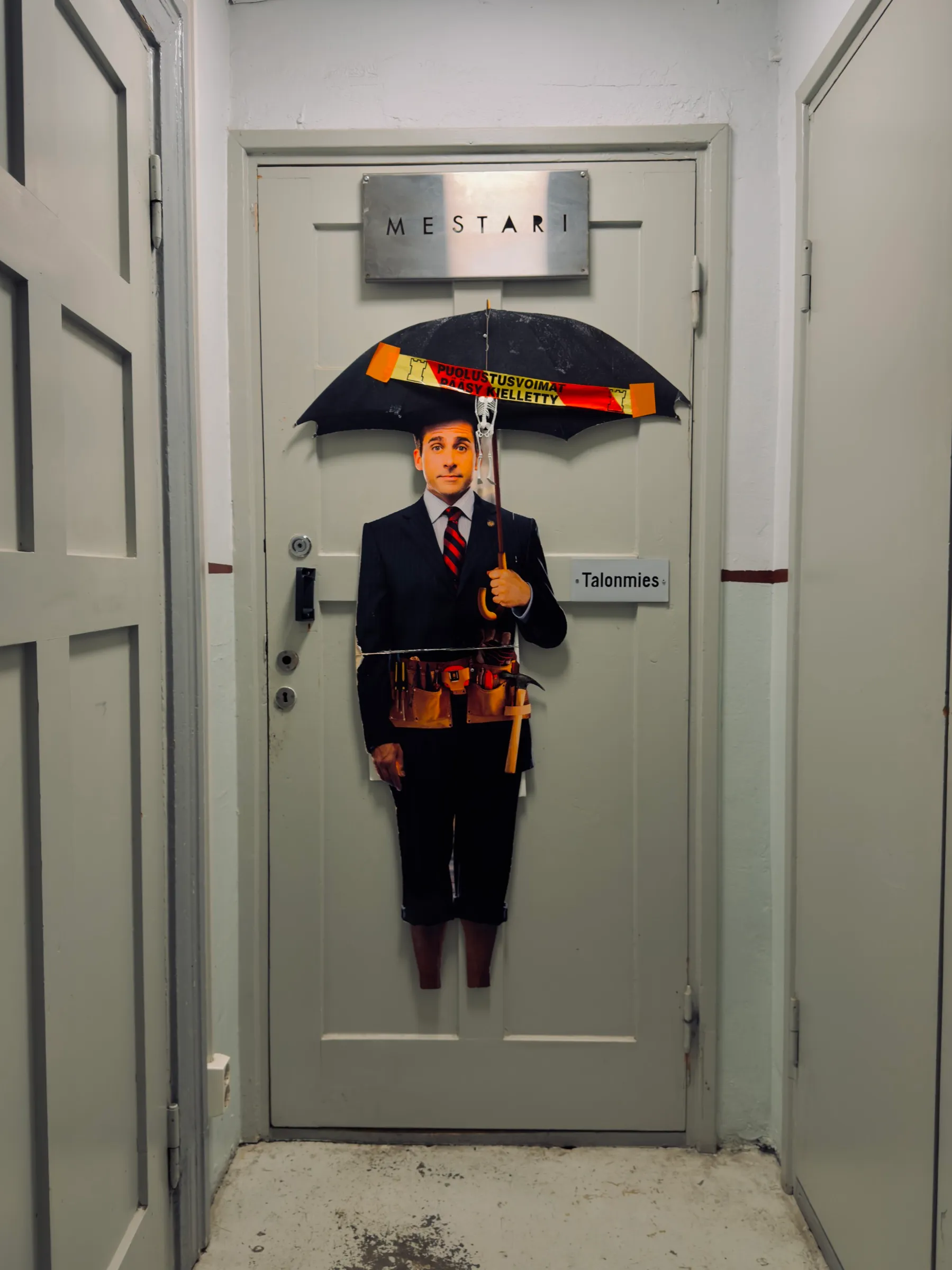 Caretaker's door labelled Talonmies, a cardboard cut-out figure with an open umbrella in front