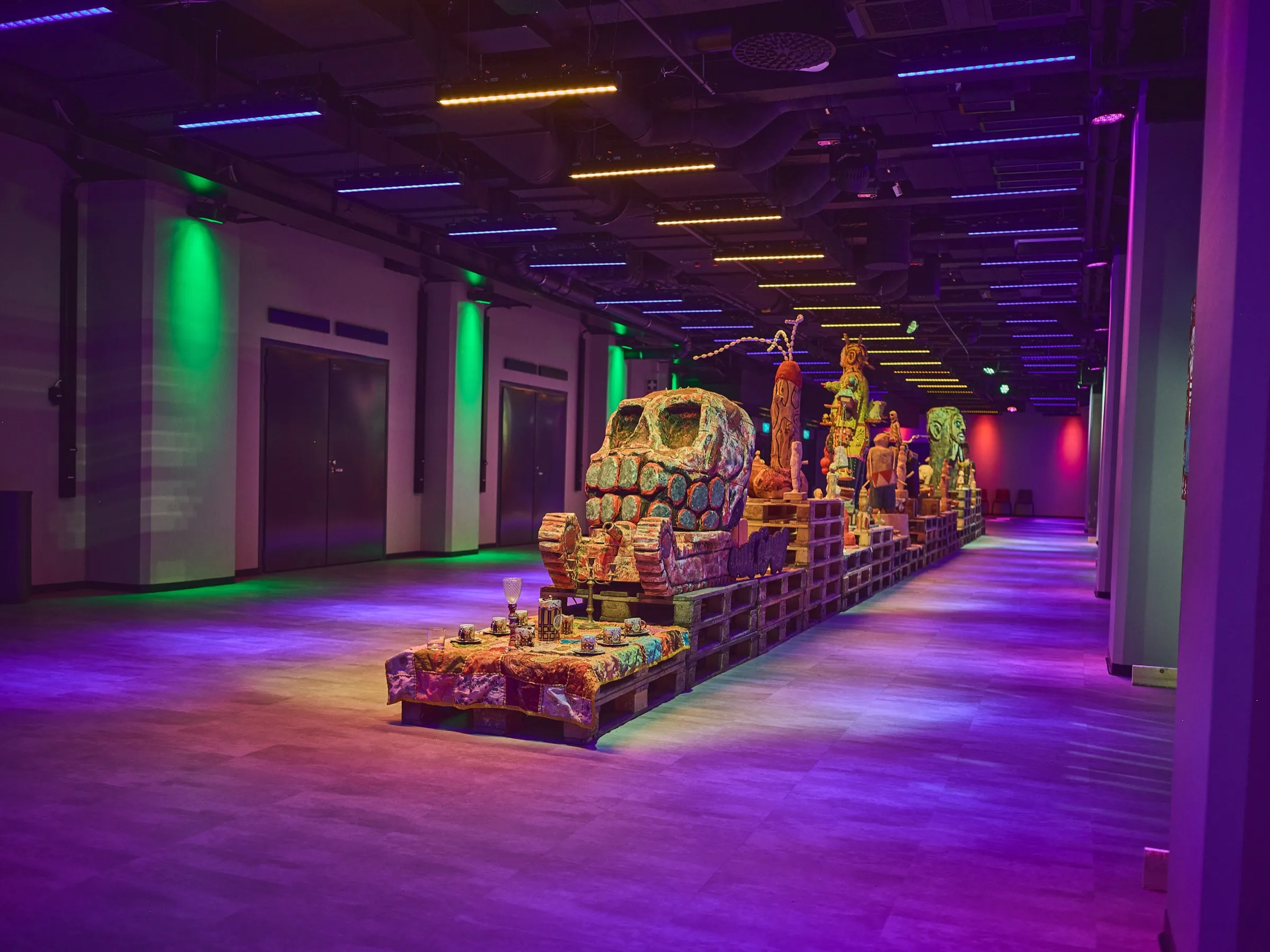 Wide view through the hall, wooden figures on pallets along the wall, blue and purple light