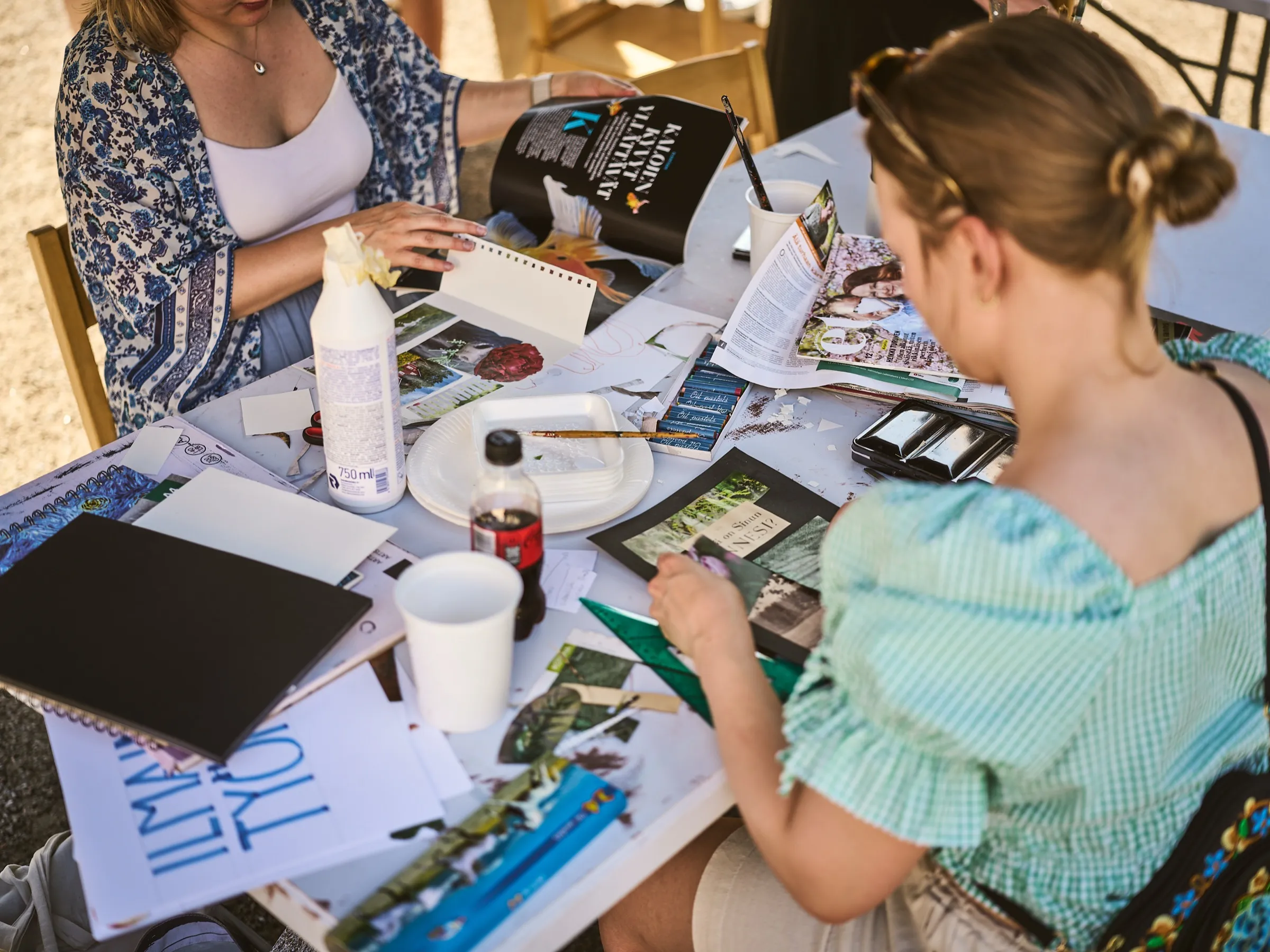 Two women at a table with oil pastels, magazines and collage material